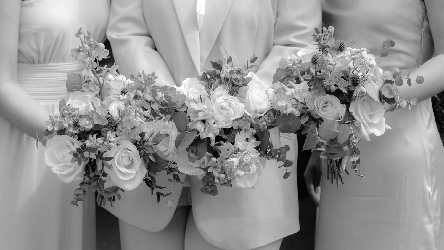 Black and white photo of bridesmaids holding elegant floral bouquets with roses and mixed flowers.