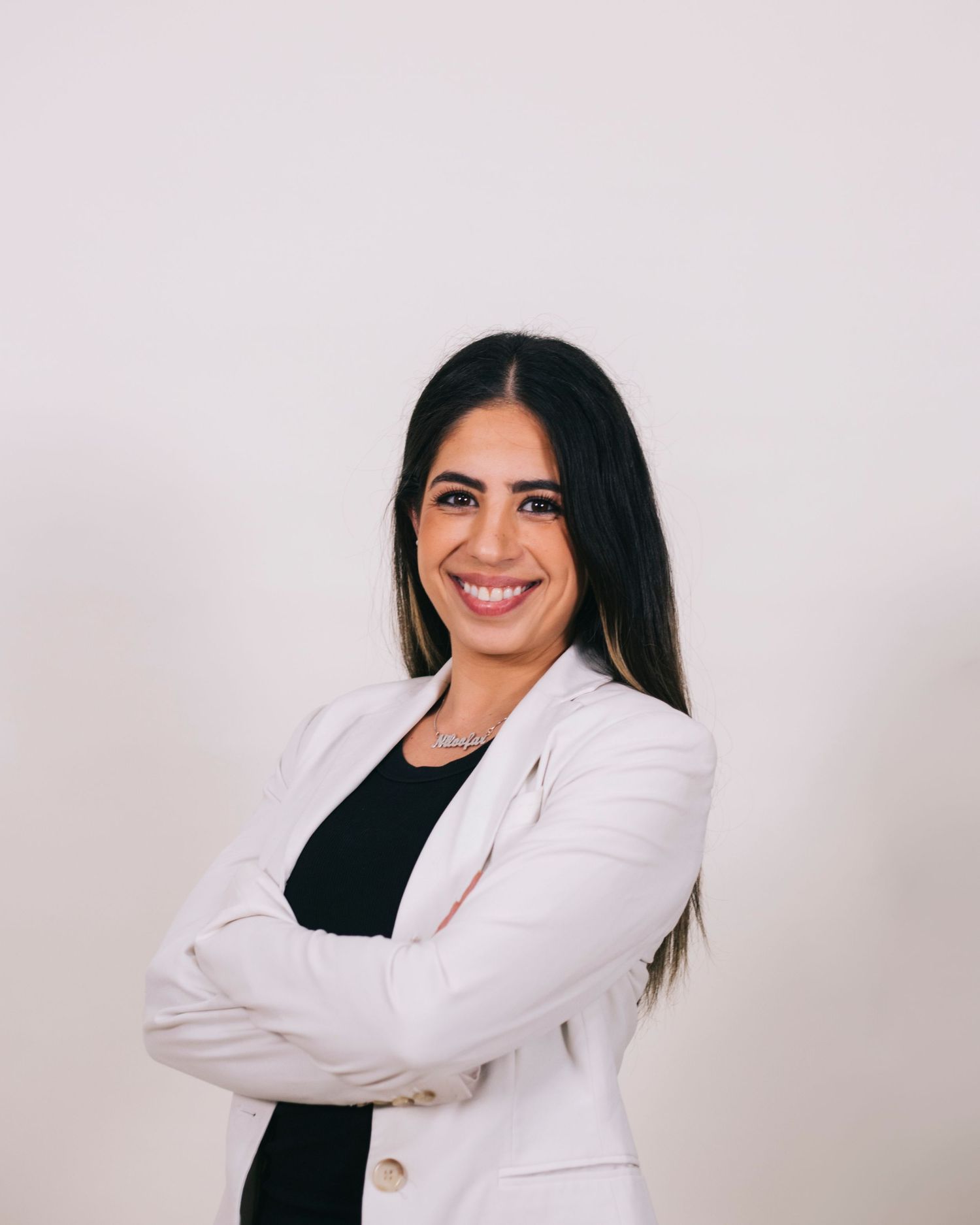 Professional woman in white blazer smiles with arms crossed against clean white background.