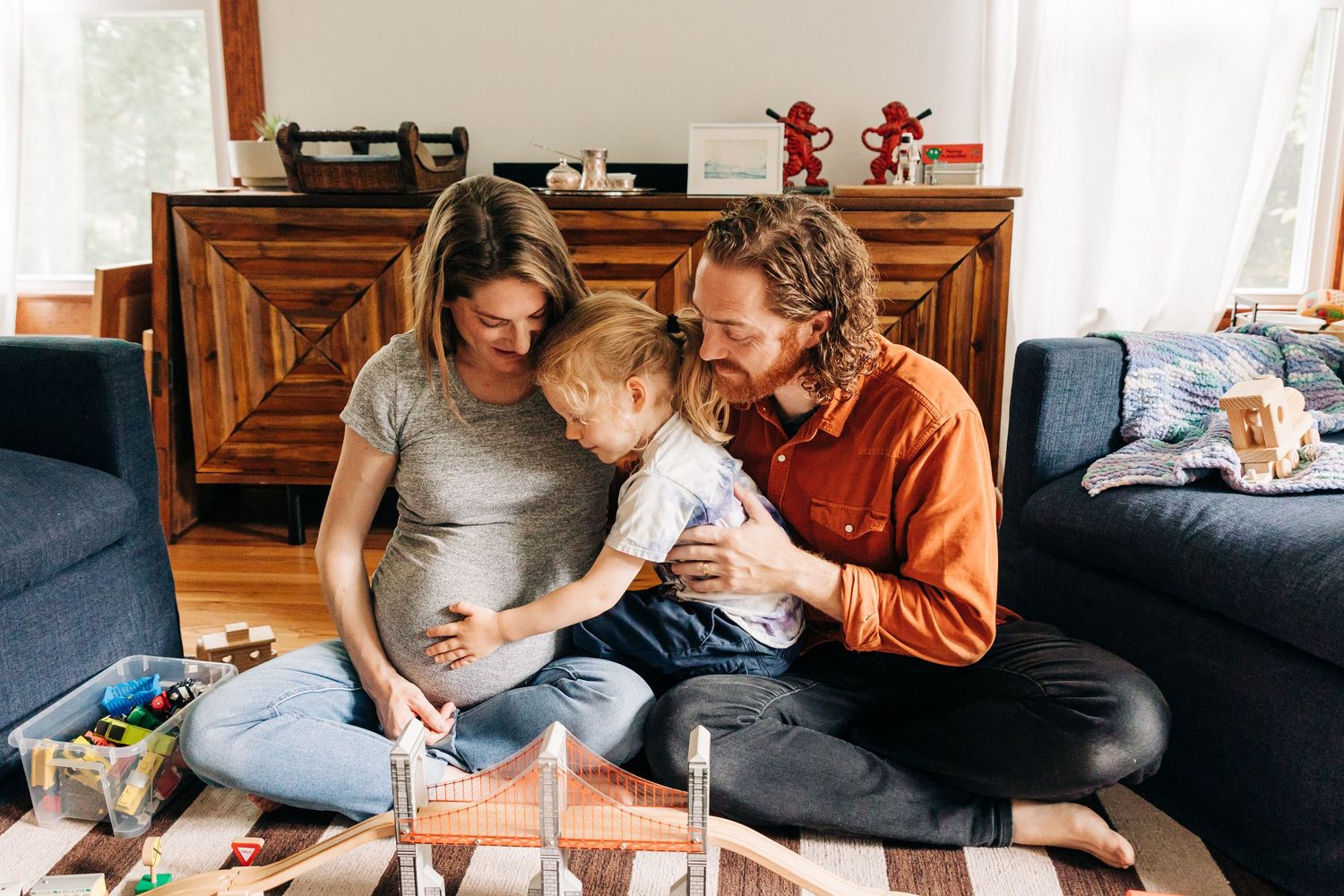 A family sits together on the floor of their living room sharing an intimate moment near scattered toys and books during maternity session.