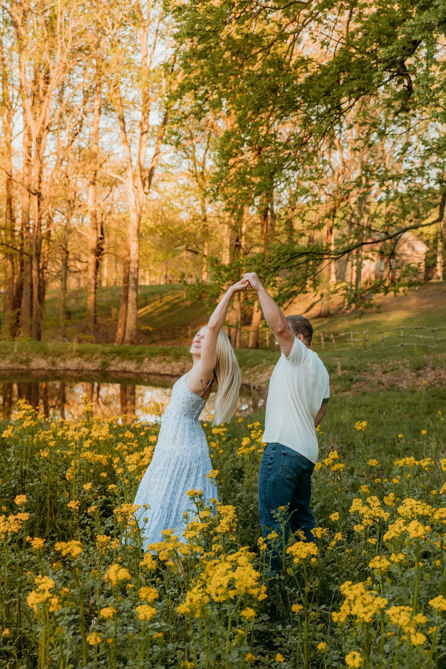 A couple dances playfully in a field of yellow wildflowers at sunset with golden autumn trees in the background.