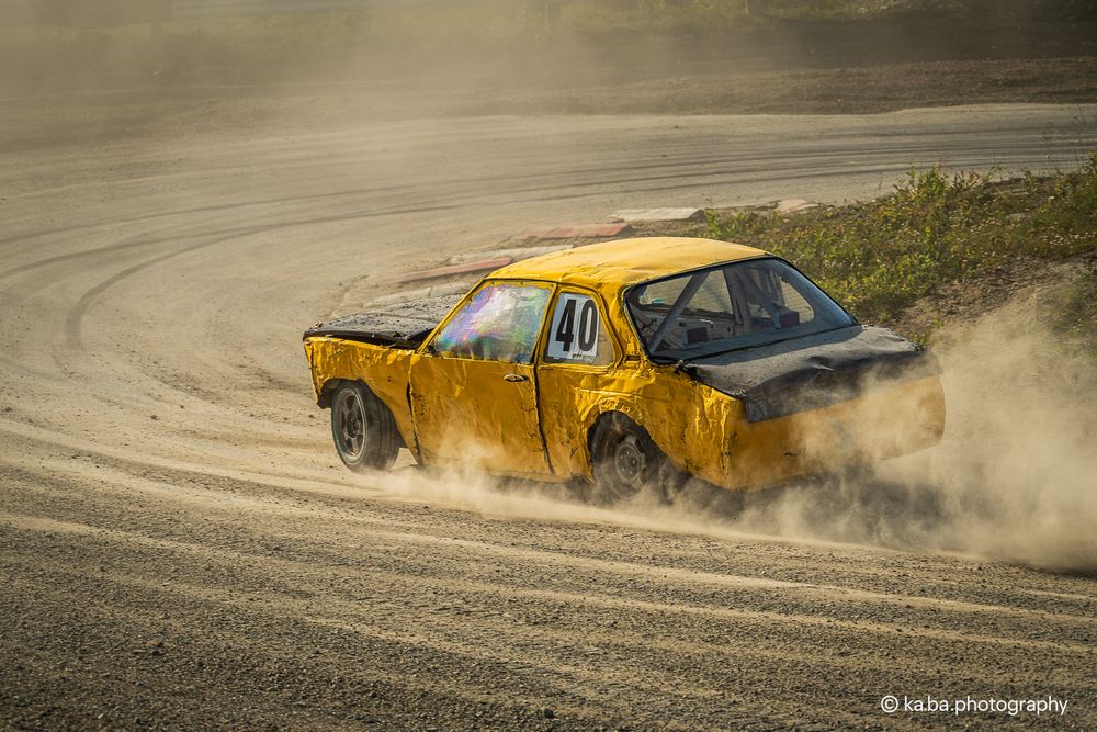 Yellow pickup truck number 40 drifting on a dusty dirt rally track at sunset.