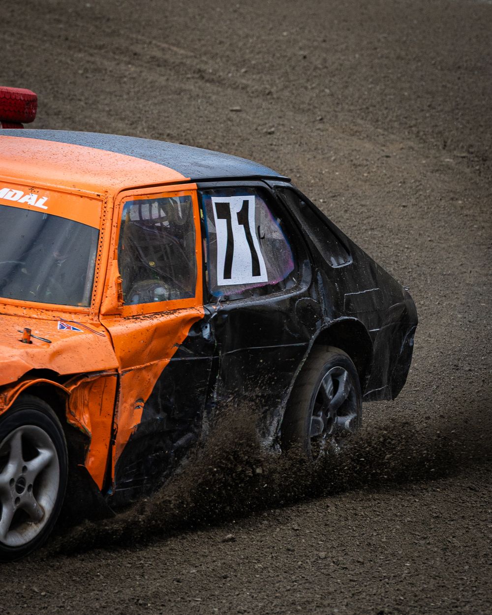 Orange and black demolition derby car number 71 sliding through dirt on a racing track.