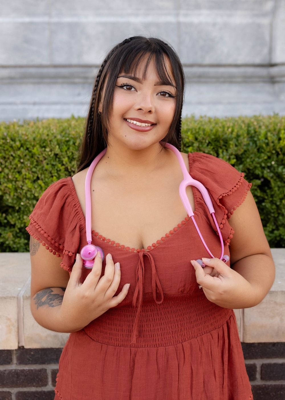True West Photography - Healthcare worker in burgundy dress holds pink stethoscope outdoors.