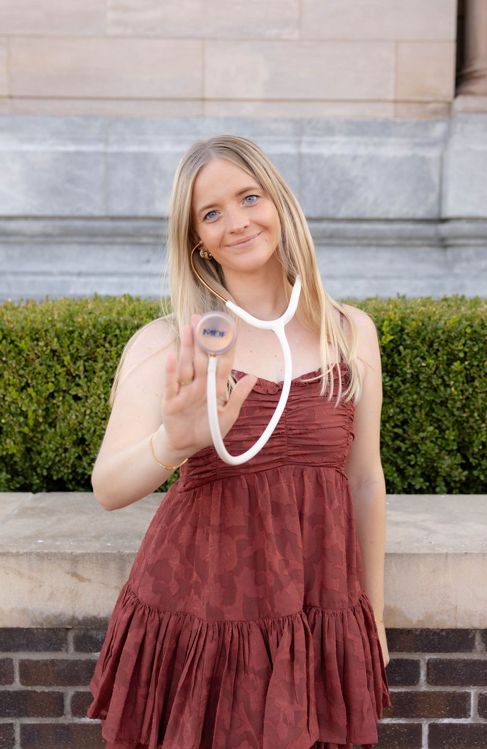 True West Photography - Healthcare professional in burgundy dress holds stethoscope while smiling outdoors.
