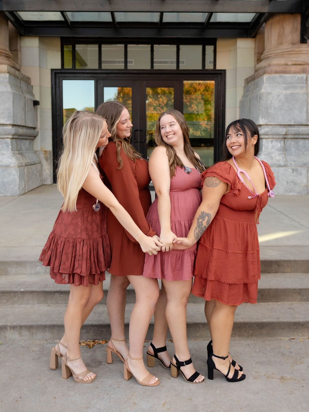 True West Photography - Four friends in matching burgundy dresses hold hands on stone steps.