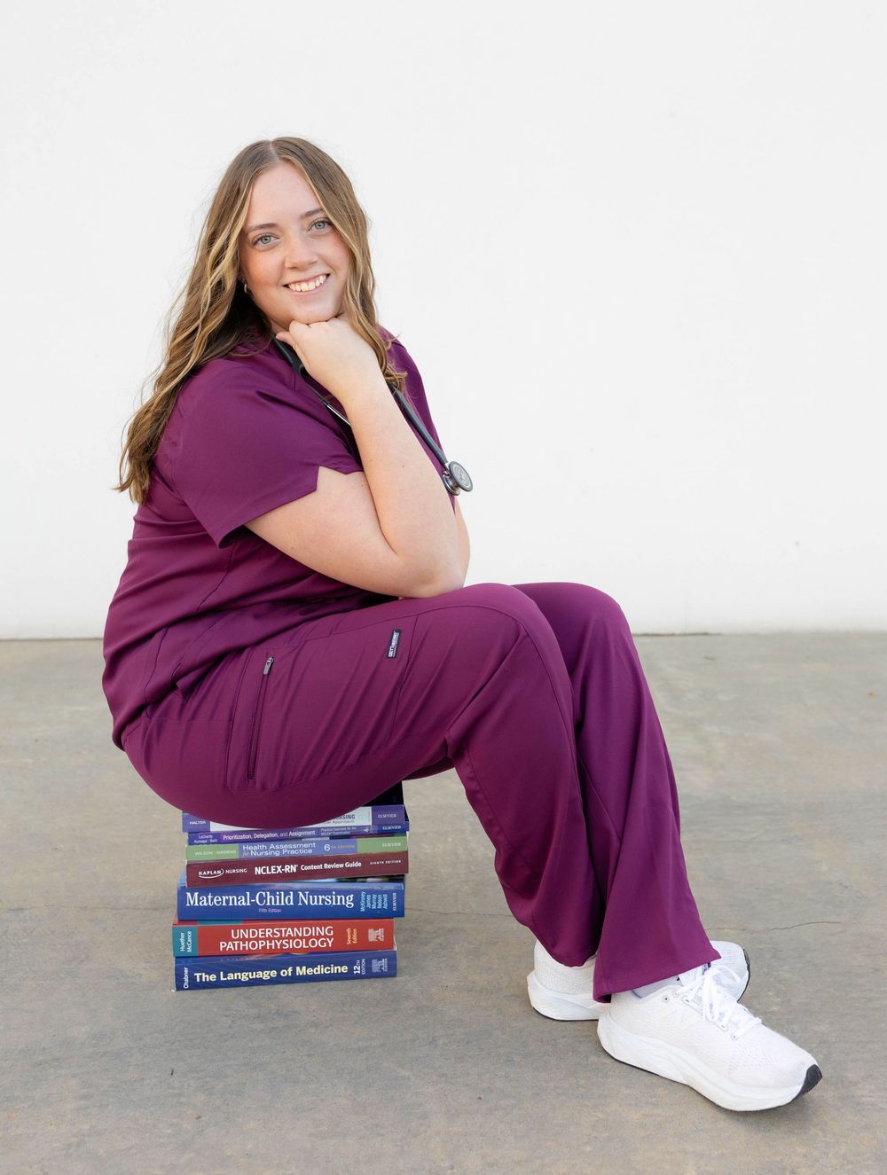 True West Photography - Medical student in purple scrubs poses with textbooks on floor in professional graduation photo series.