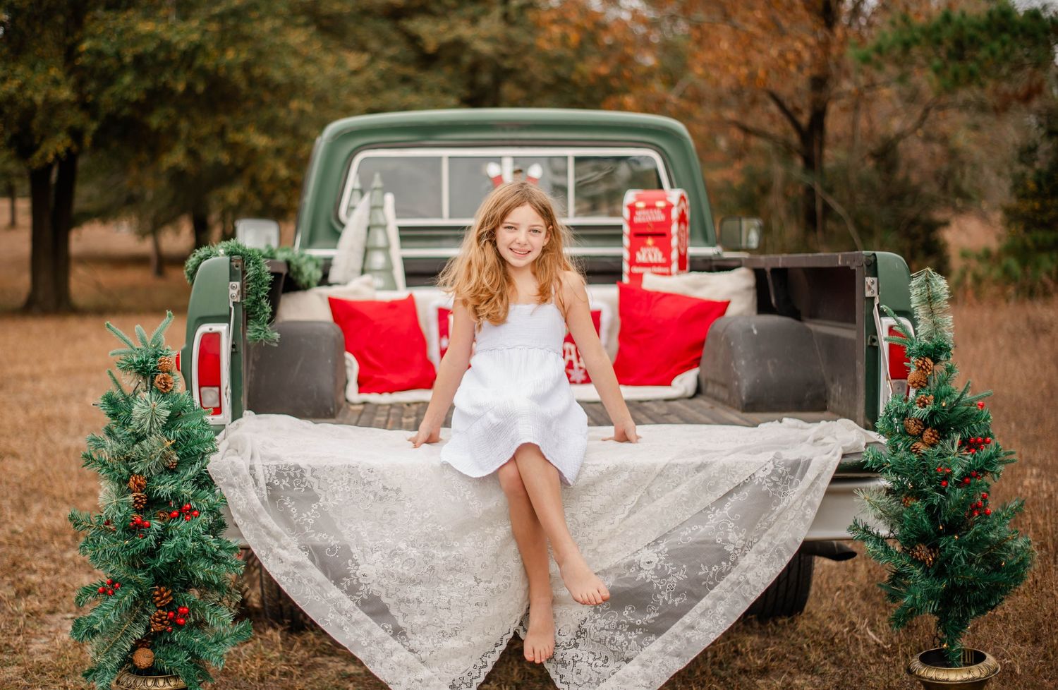 A bride in a flowing white lace gown poses gracefully in an autumn outdoor setting with red and green accents.