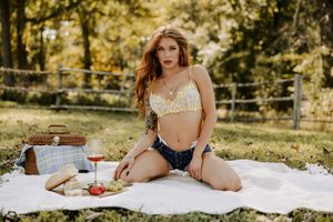 Summer garden picnic with wine glasses and fresh fruit arranged on white blanket.