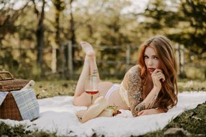 Outdoor picnic themed boudoir photo with model on white blanket near vintage basket.