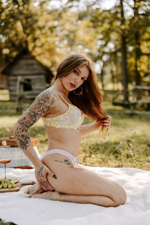 Artistic boudoir photography session on white blanket outdoors with golden autumn lighting and trees in background.