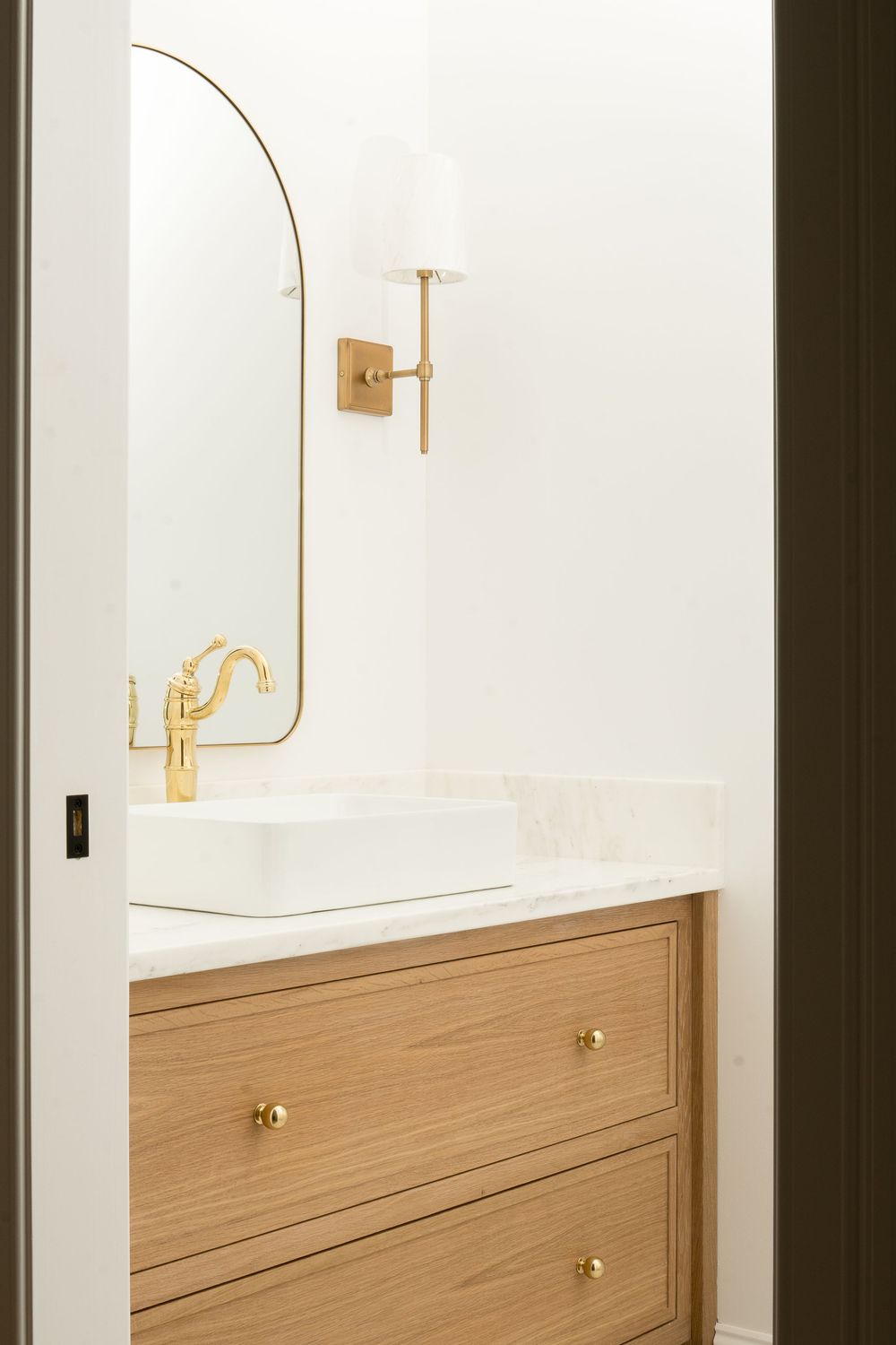 Minimalist bathroom interior with wooden vanity and brass wall sconces.