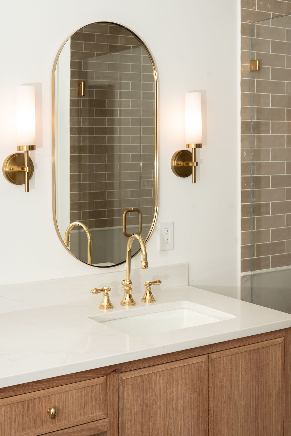 Elegant bathroom design featuring gold accents, oval mirror, and grey subway tile backsplash.