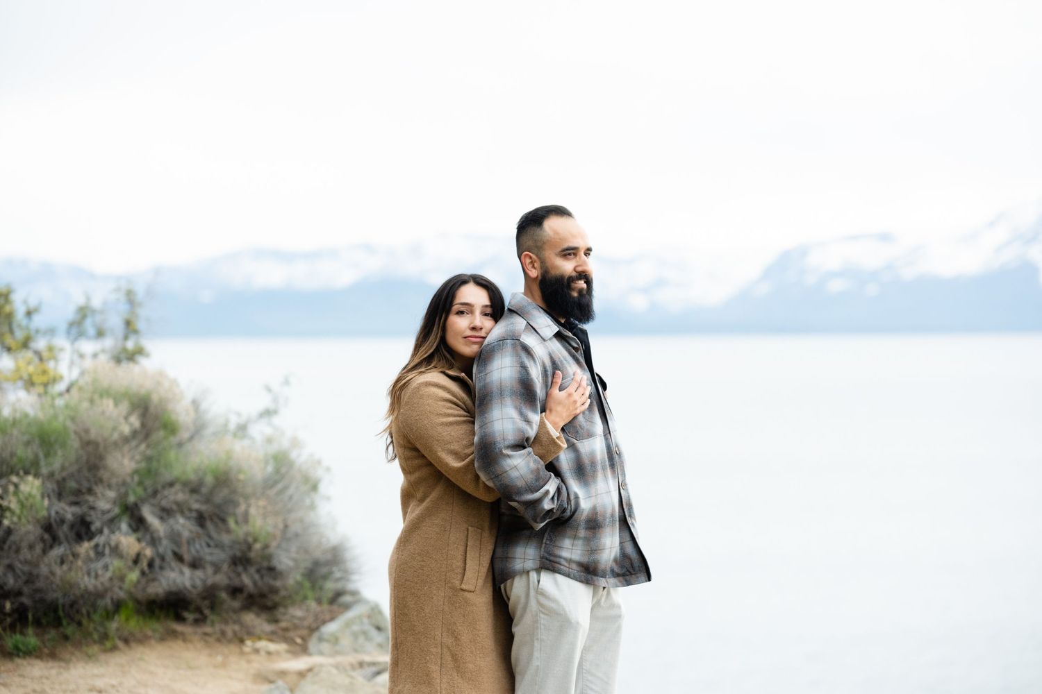 Couple enjoying a romantic moment while lying on sandy beach with snowy mountains in background.