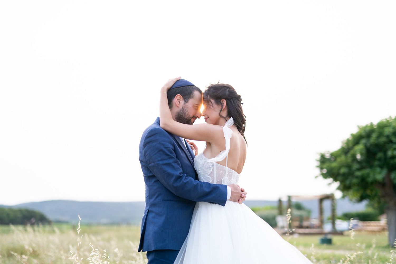 Jeunes mariés s’embrassant dans un champ, portrait romantique au coucher du soleil.