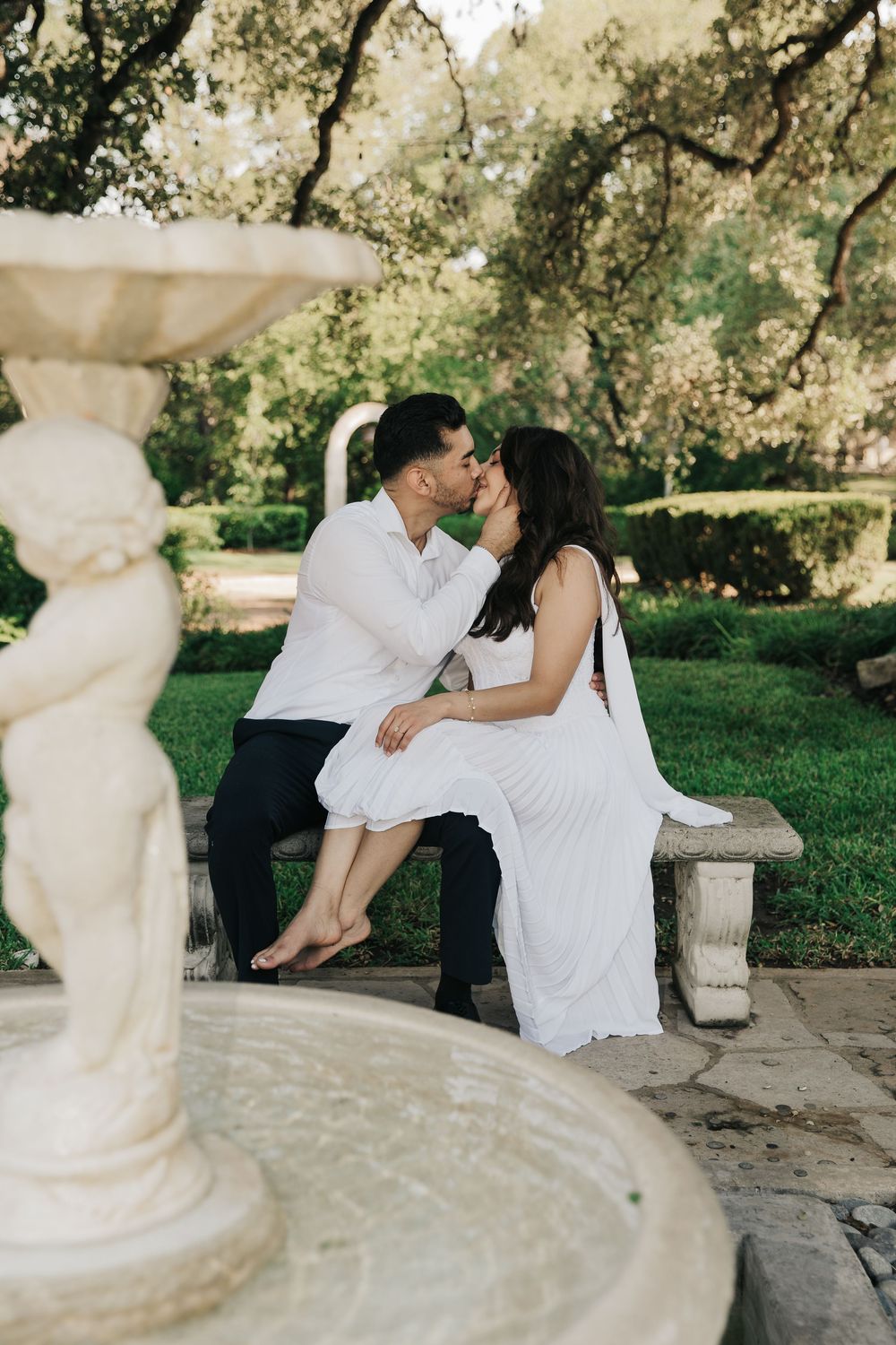 A romantic photo series of a couple in white clothing sharing tender moments while sitting on a stone ledge outdoors.
