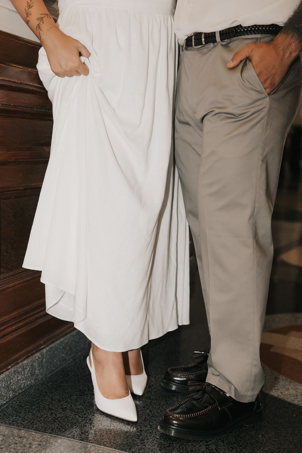 Cropped view of elegant wedding attire showing white dress and gray pants with formal shoes on wooden floor.