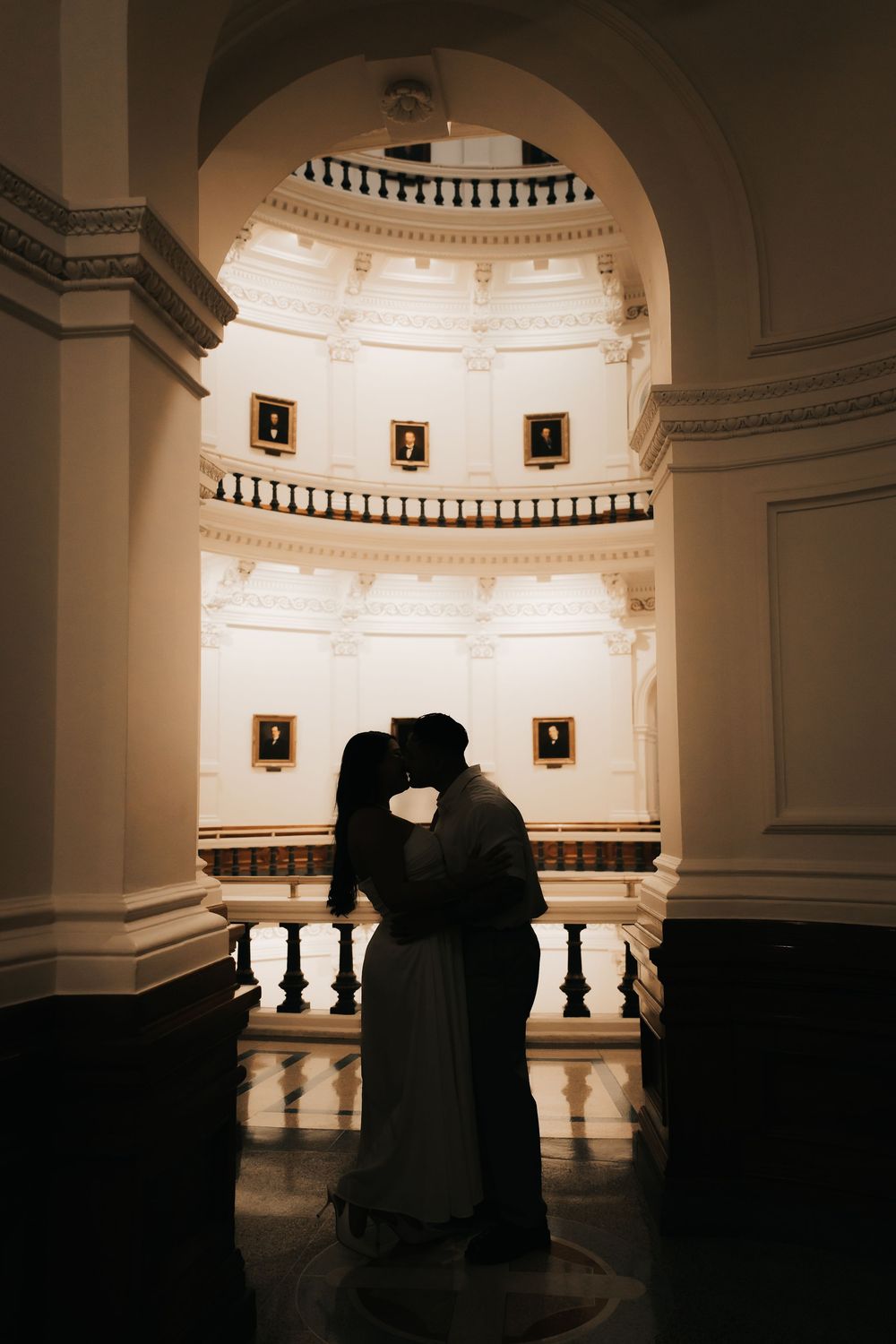 A romantic silhouette of two figures embracing in a dimly lit historic building with arches and ornate architecture.