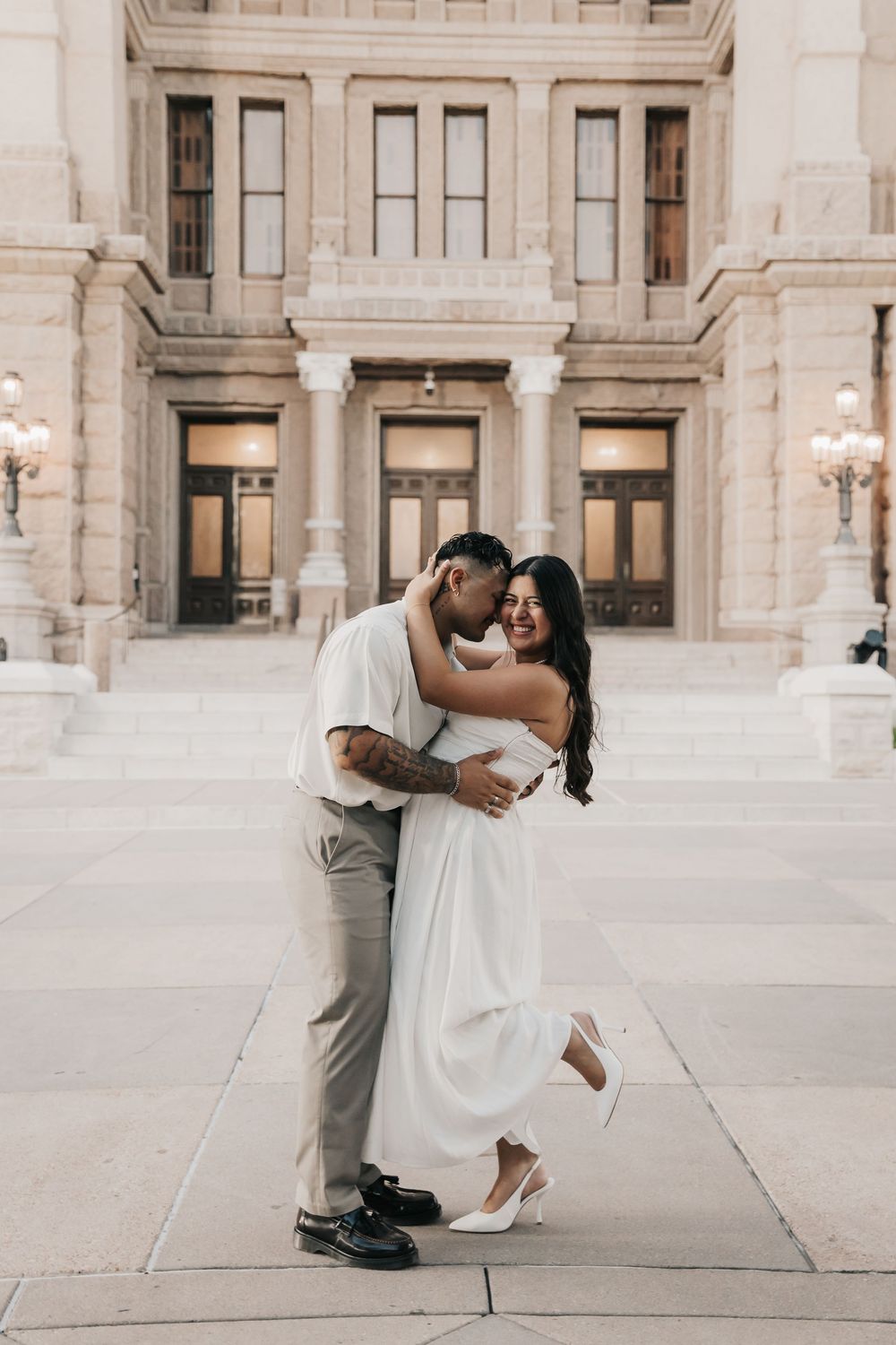 A romantic moment captured in an elegant architectural setting with white stone columns and natural lighting.