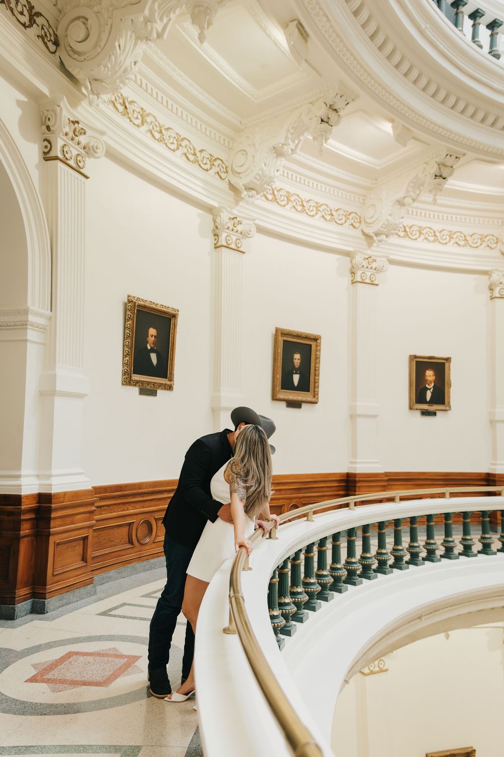 A couple shares a romantic moment in an elegant curved hallway with white walls and ornate architectural details.