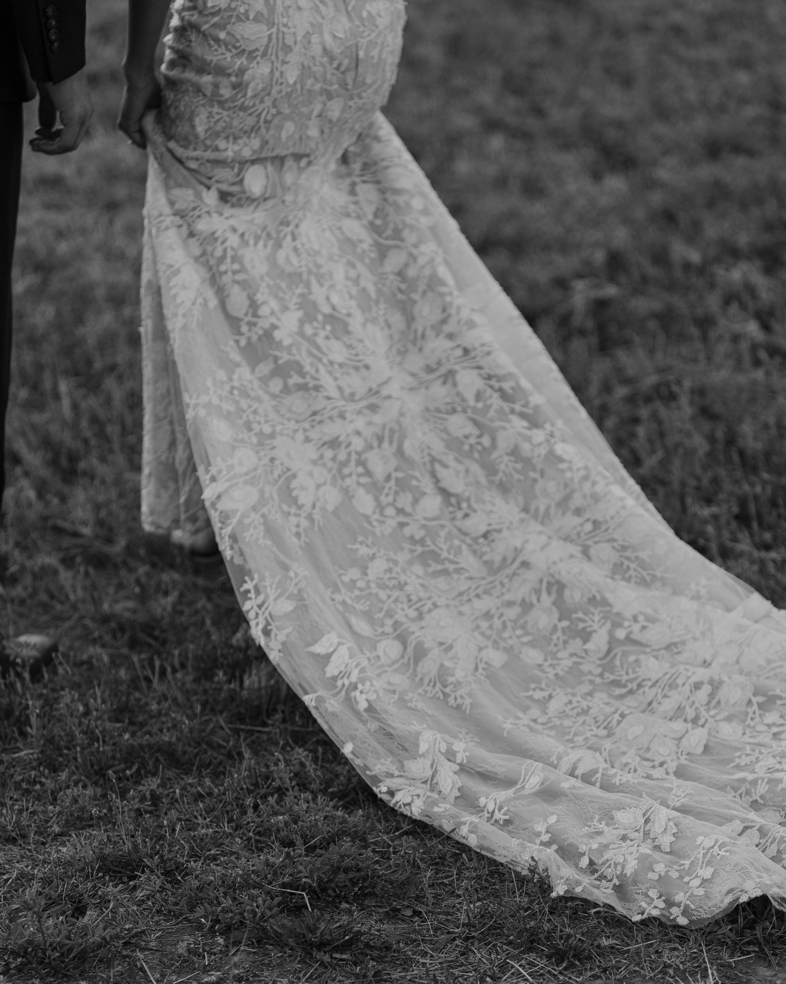 A detailed close-up sequence showing the delicate lace and beading on the train of a white wedding dress on grass.