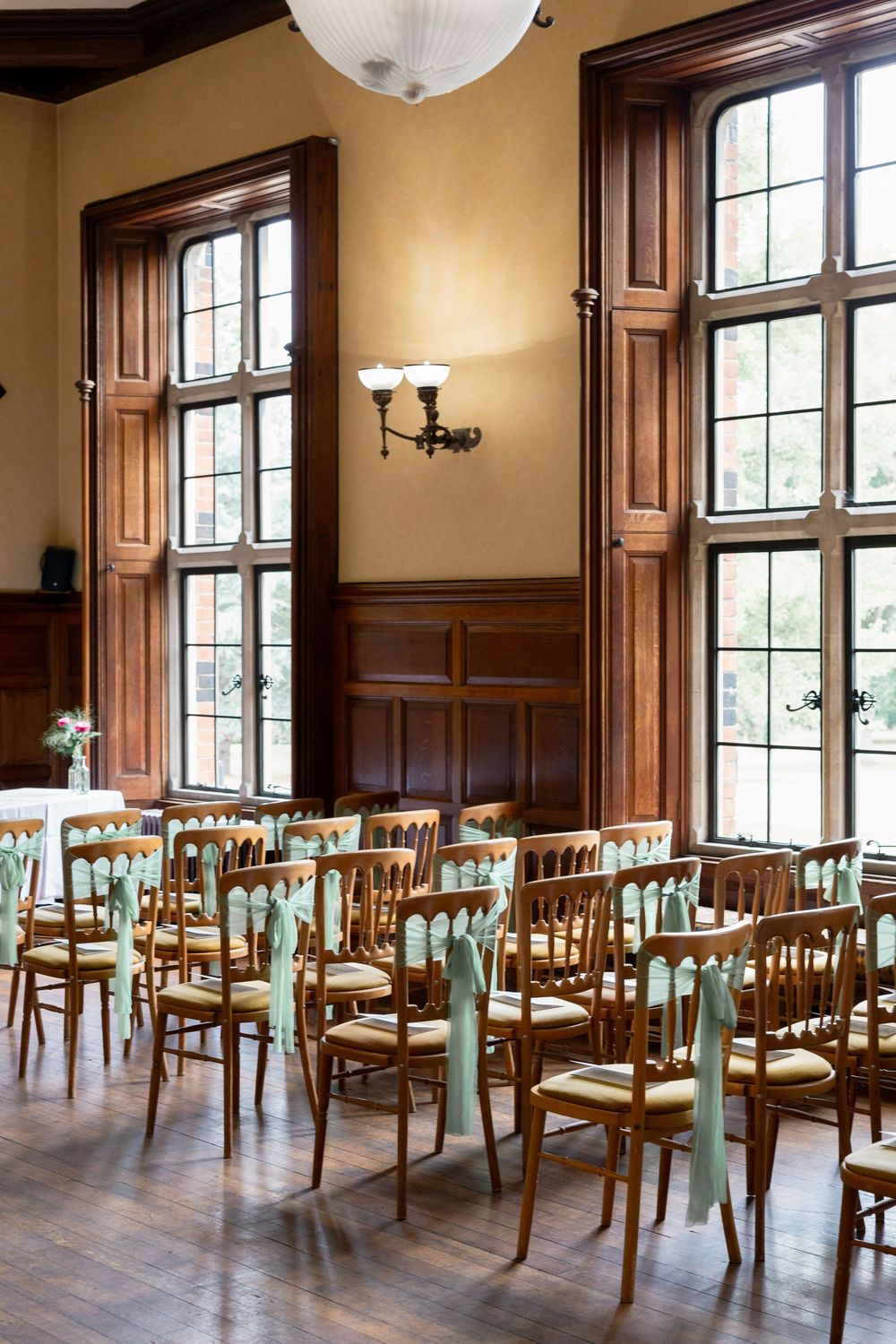 Elegant Oak Room at The Elvetham wooden trim windows, mint green chairs arranged in rows, and classic wall sconces on beige walls.