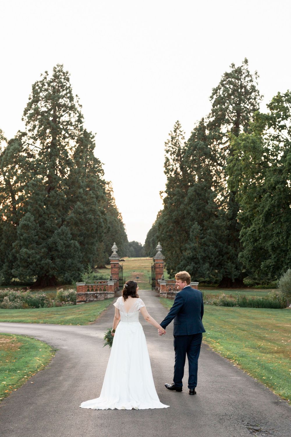 A bride and groom walk hand in hand down a tree-lined path at The Elvetham during their outdoor wedding photo session.