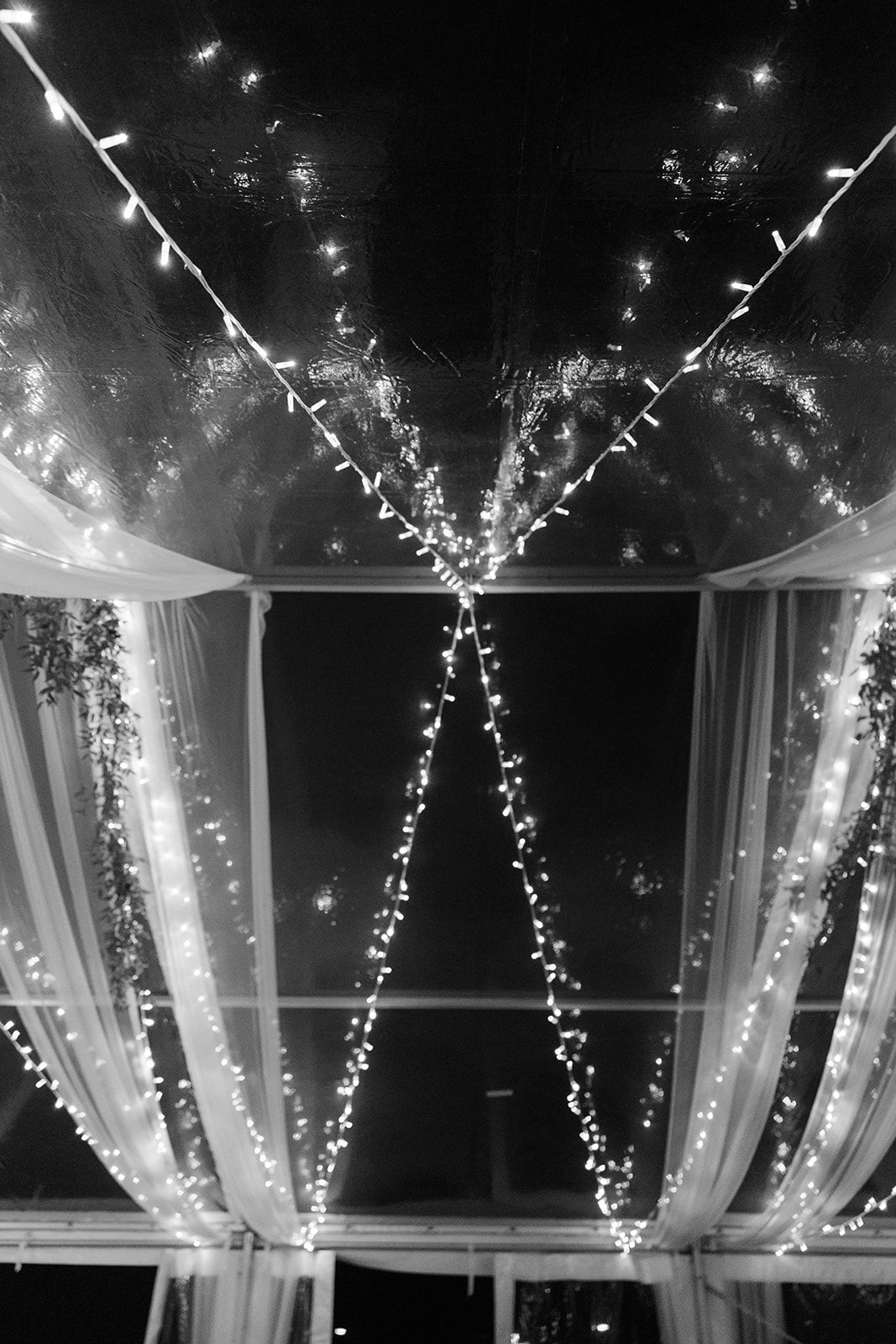 Elegant white fabric drapes and twinkling string lights create a romantic ceiling canopy decoration for an indoor event.