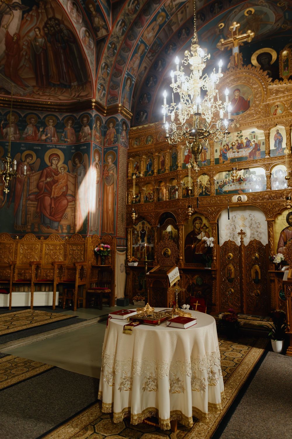 Interior of an ornate Orthodox church with crystal chandeliers and a white-clothed altar table in warm lighting.