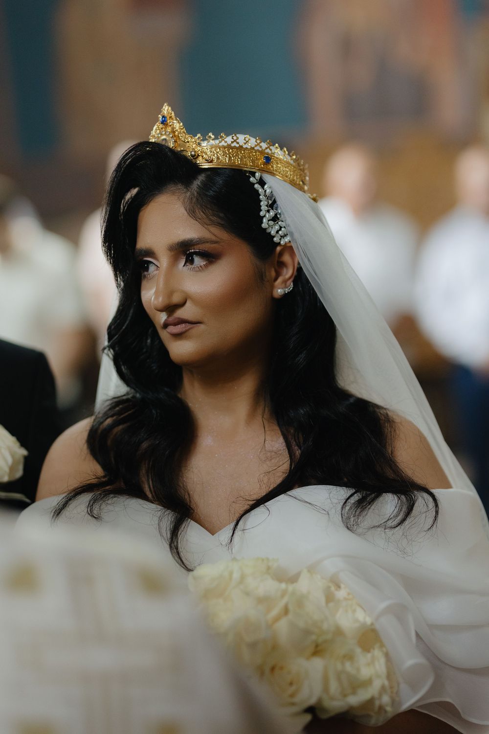 A bride in a white dress and golden crown veil looks off to the side with a dreamy expression.