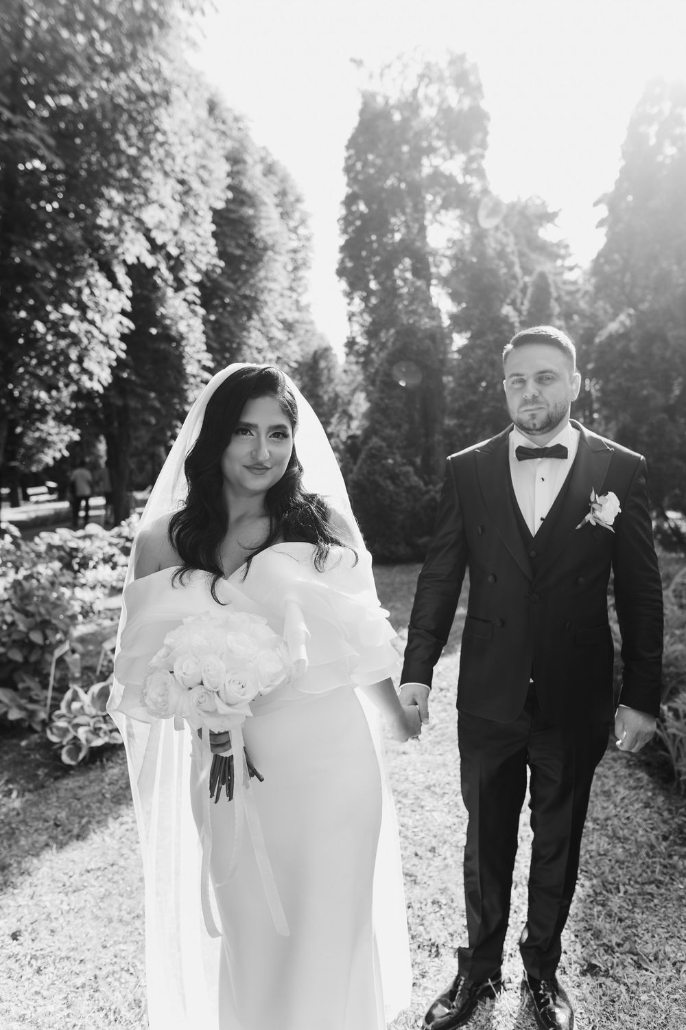 A black and white wedding photo series showing a couple walking together in a scenic outdoor garden setting.