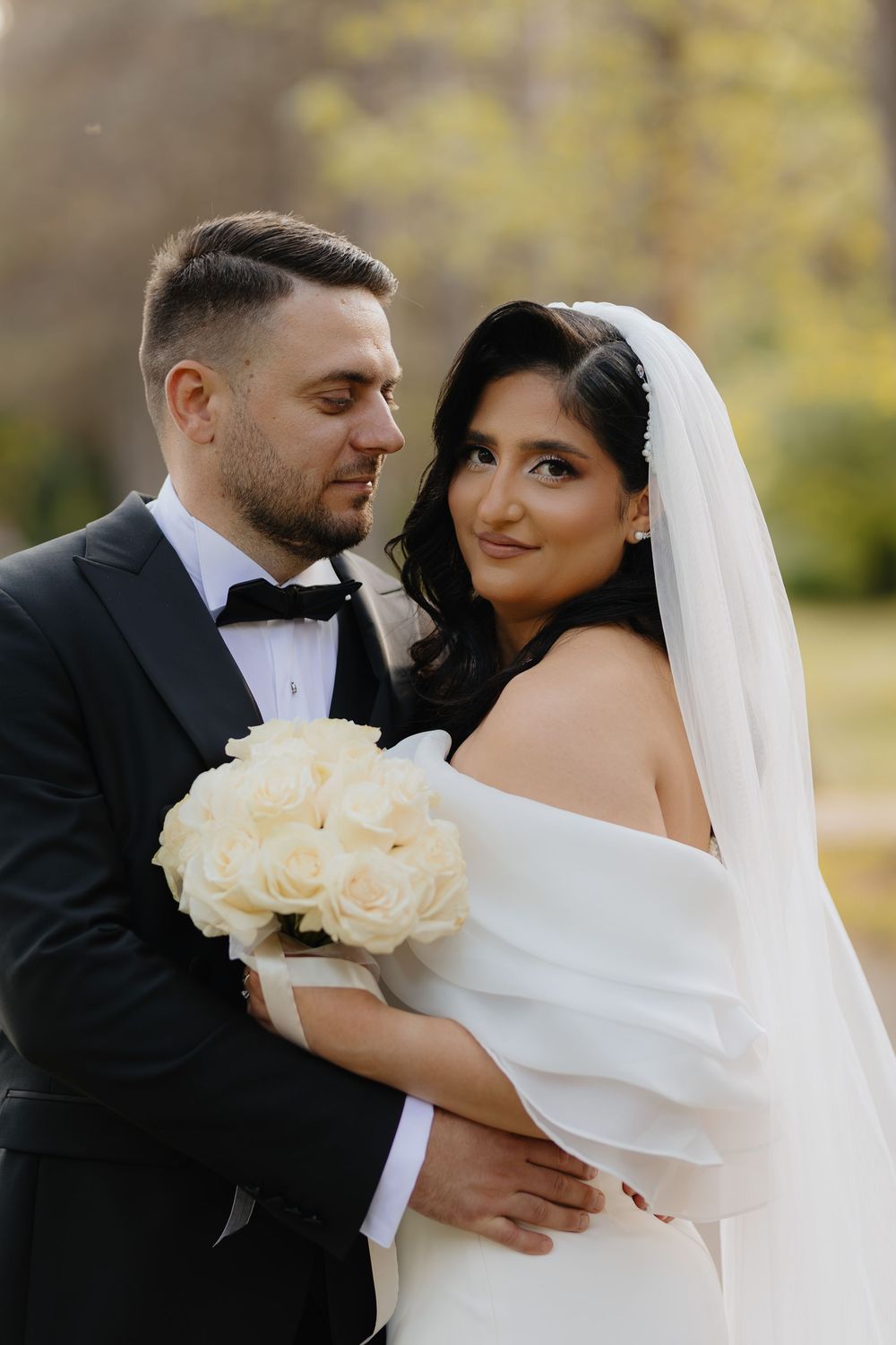 Romantic wedding couple embraces outdoors in autumn with white roses and flowing veil.