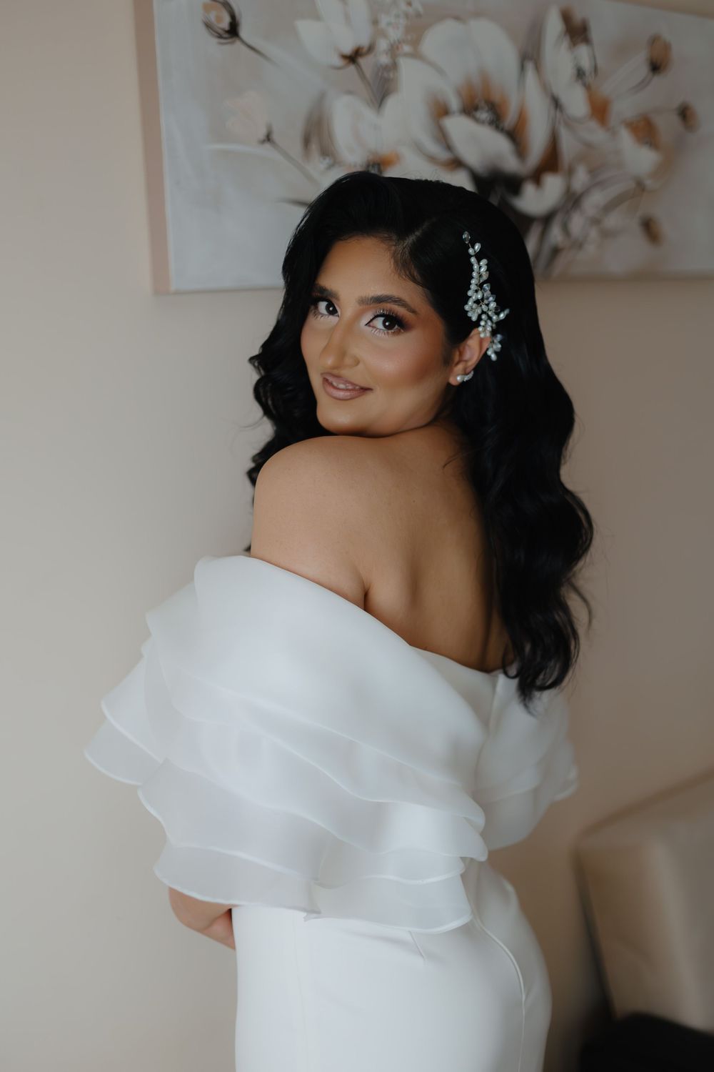 A stunning off-shoulder white wedding dress with layered ruffles and delicate crystal hair accessories.