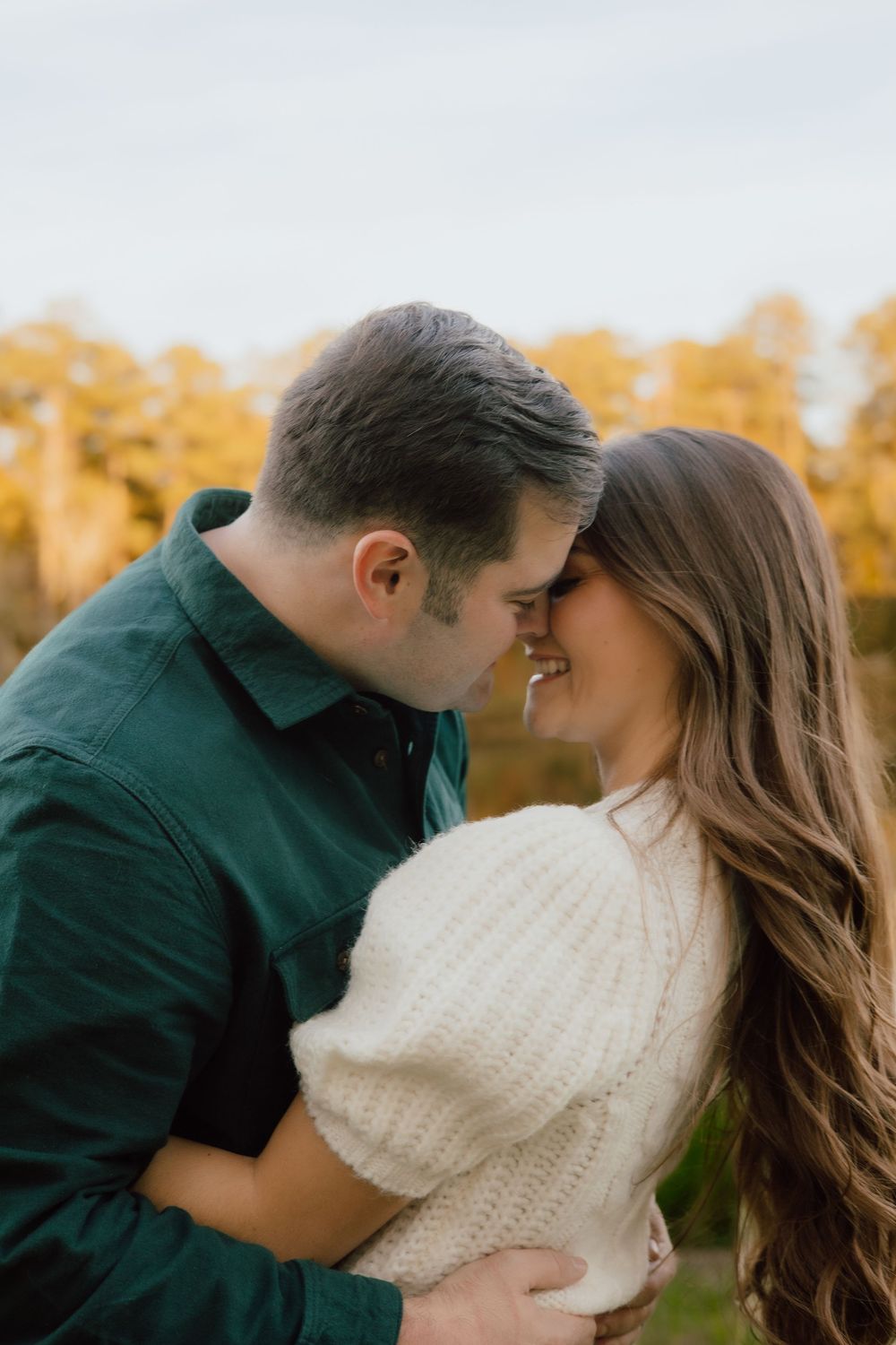 A romantic couple sharing an intimate moment while embracing outdoors during autumn with golden trees in background.