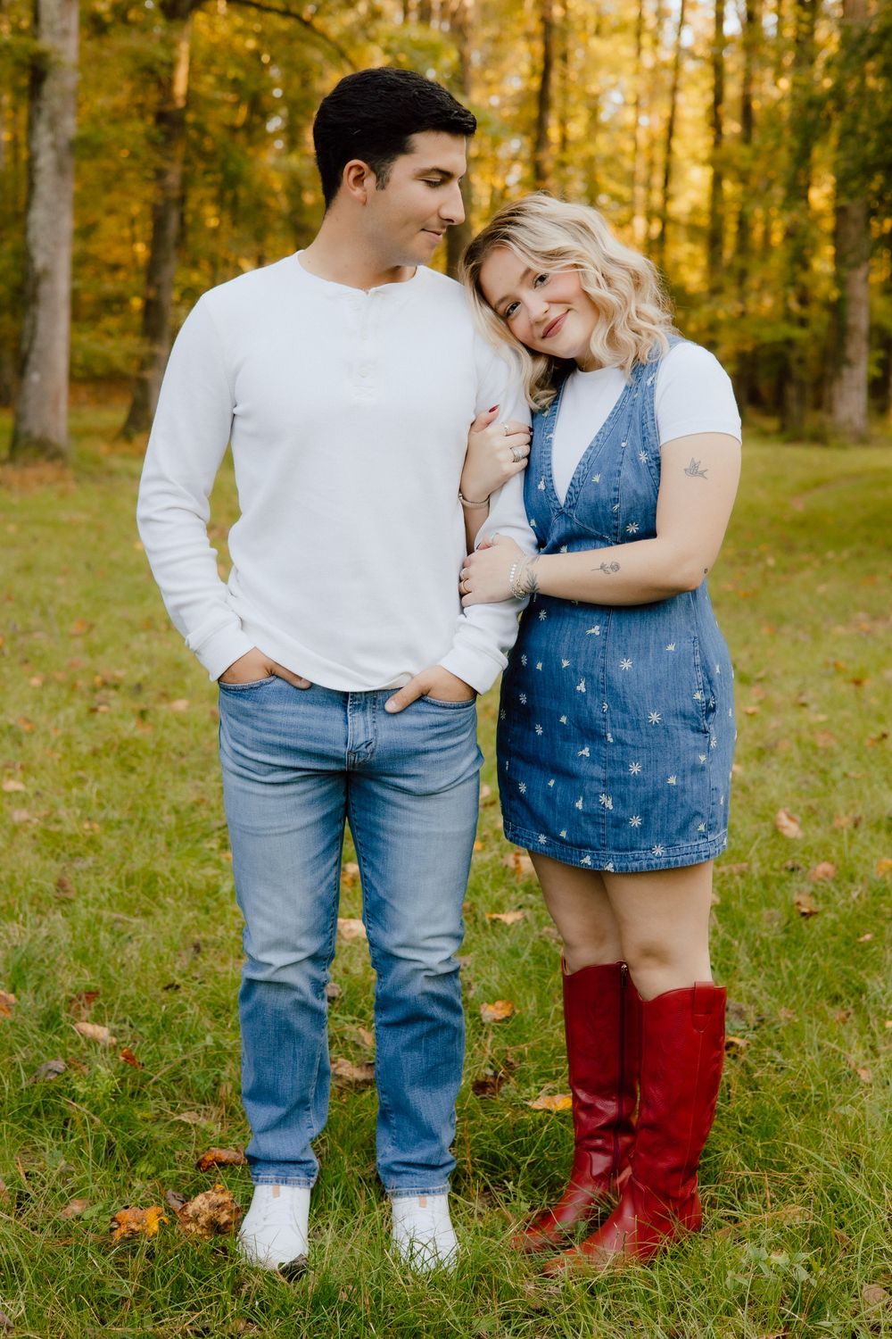 A couple in casual denim outfits and boots share an intimate moment in a sunlit autumn forest setting.