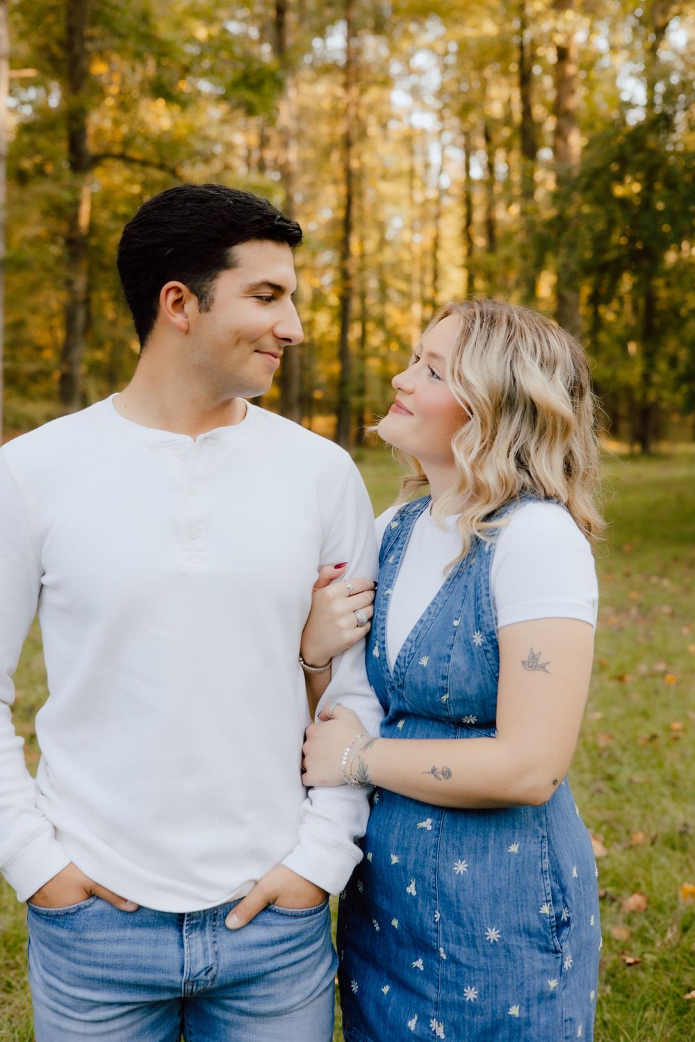 Couple in casual white shirts and denim share intimate moments in a sunlit autumn forest setting.