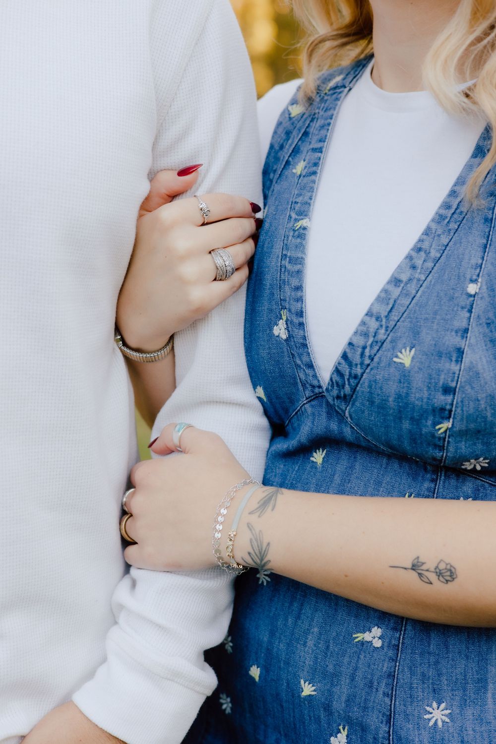 Close-up details of denim and white clothing with delicate floral embroidery and visible tattoo artwork.
