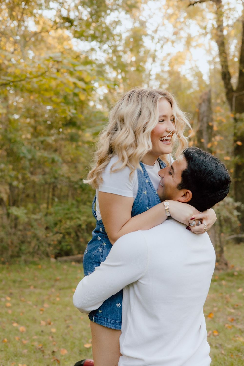 A joyful couple embraces in an autumn forest setting with golden leaves in the background.