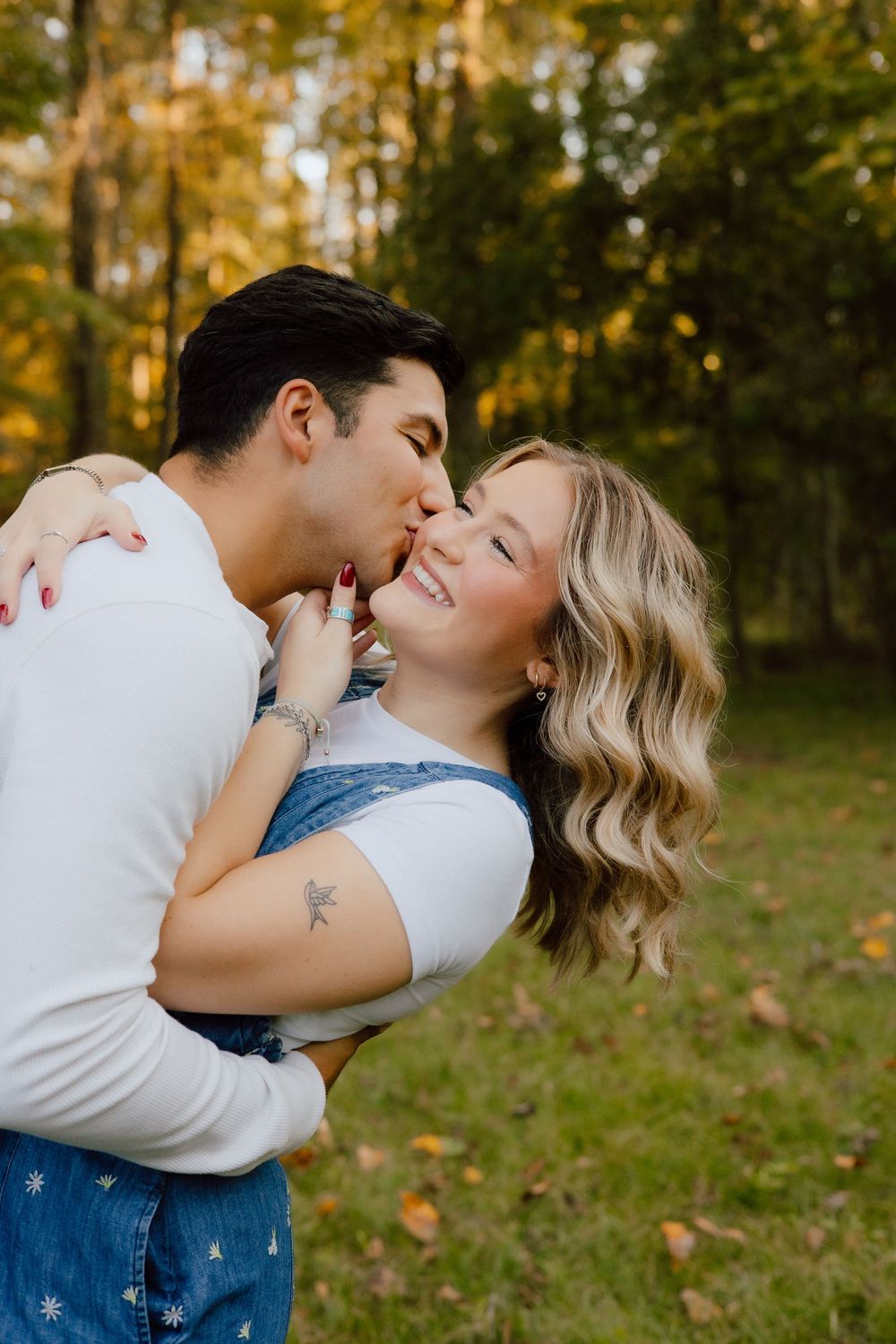 A romantic moment between a couple sharing laughter and affection in a wooded fall setting.
