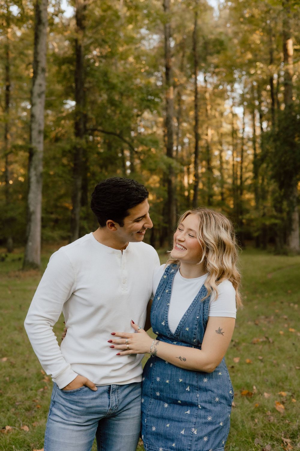 A couple shares a tender moment while standing together in a forest during autumn.
