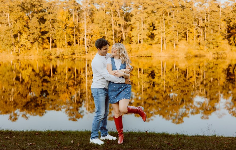 A couple shares a tender moment in a golden autumn setting by a reflective lake.