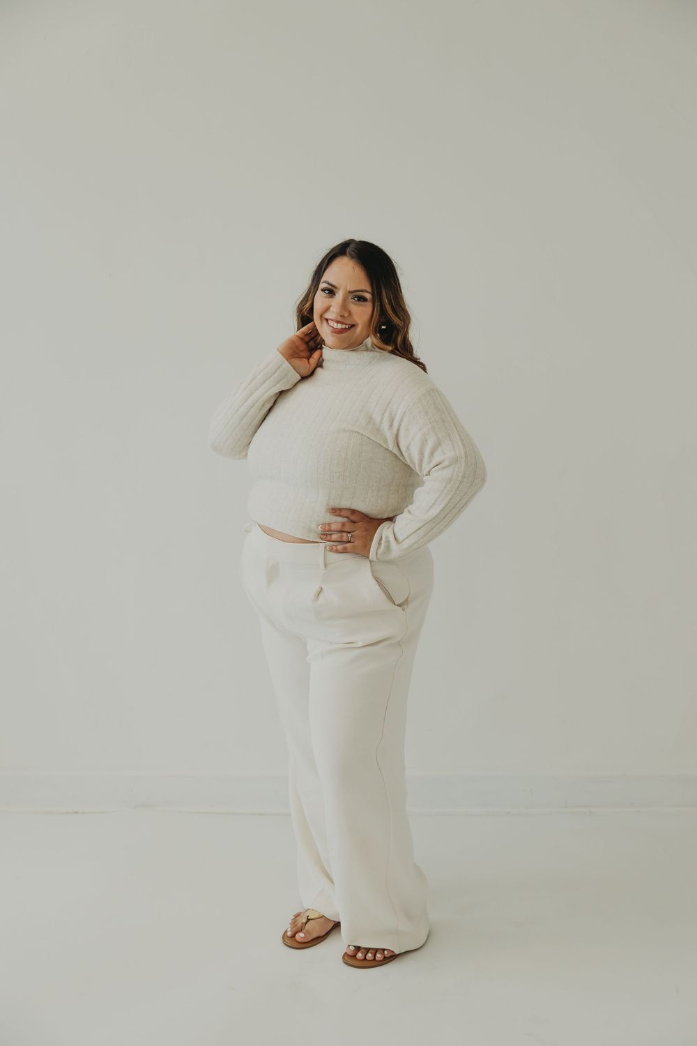 A person wearing a cozy cream-colored sweater and matching pants poses playfully against a white studio background.