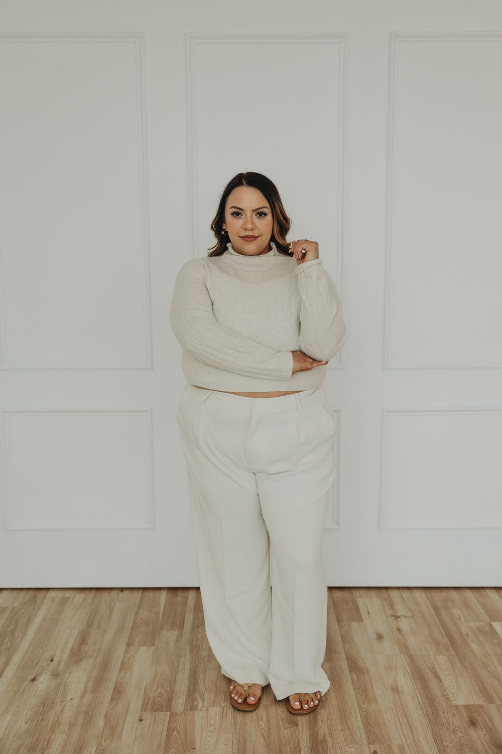 A model in a cozy cream-colored sweater and matching pants poses against a white wall in a minimalist setting.