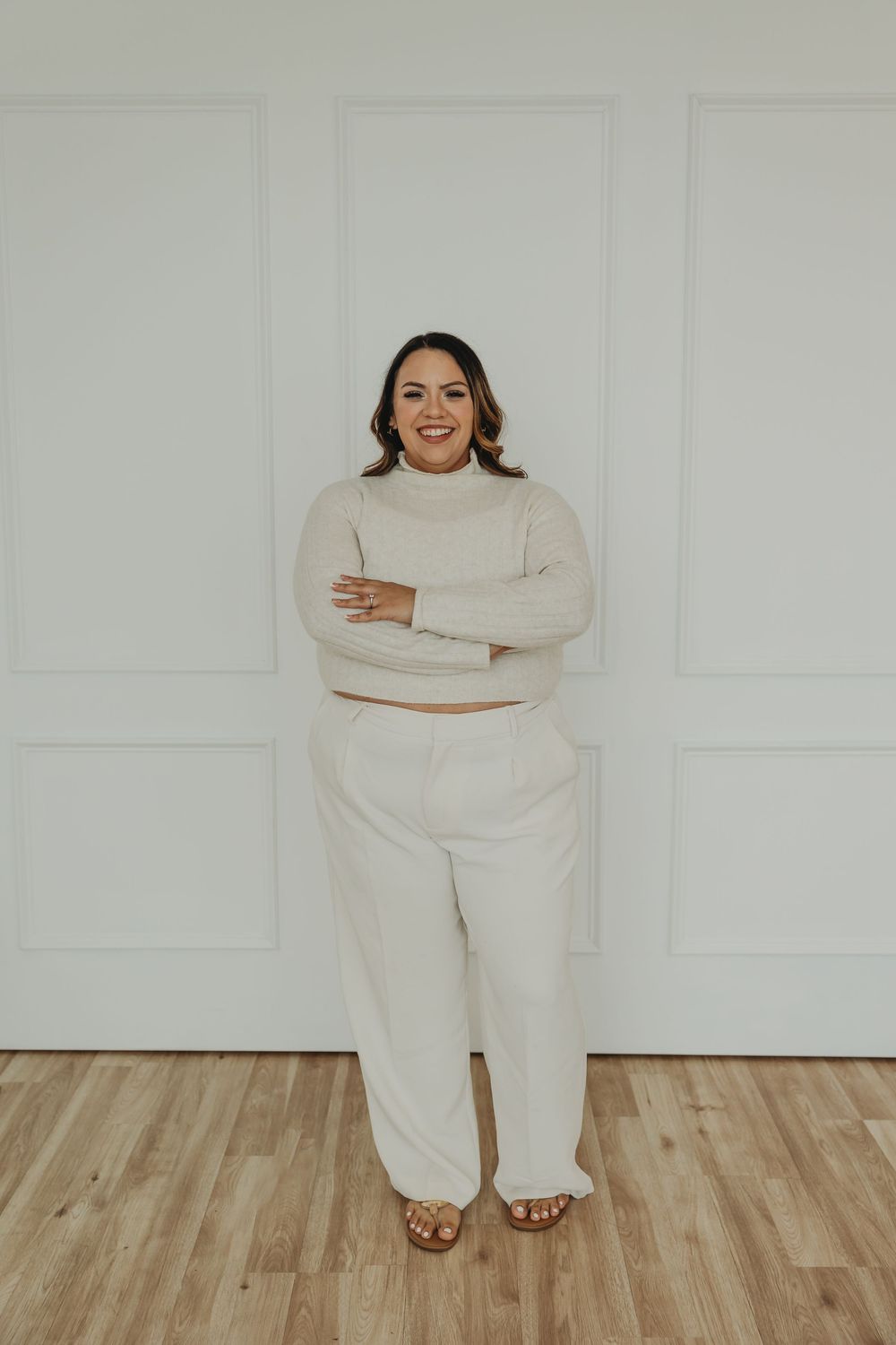 A person wearing an all-white outfit with a turtleneck sweater and wide-leg pants poses against a white wall.