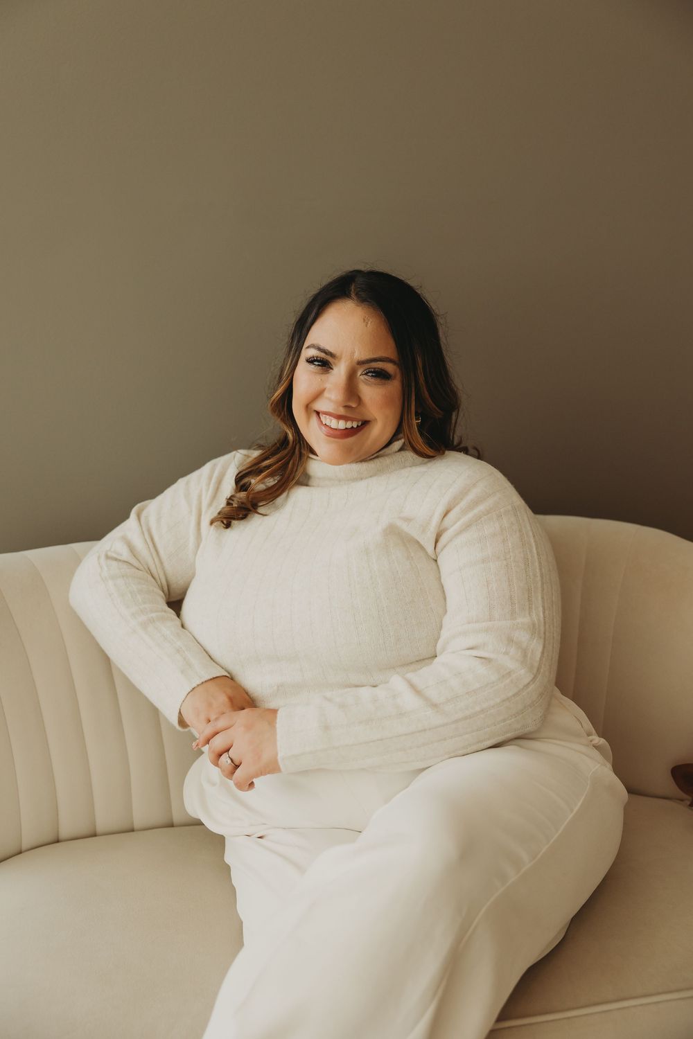 A person wearing a cozy white sweater lounges comfortably on a cream-colored sofa in a minimalist setting.