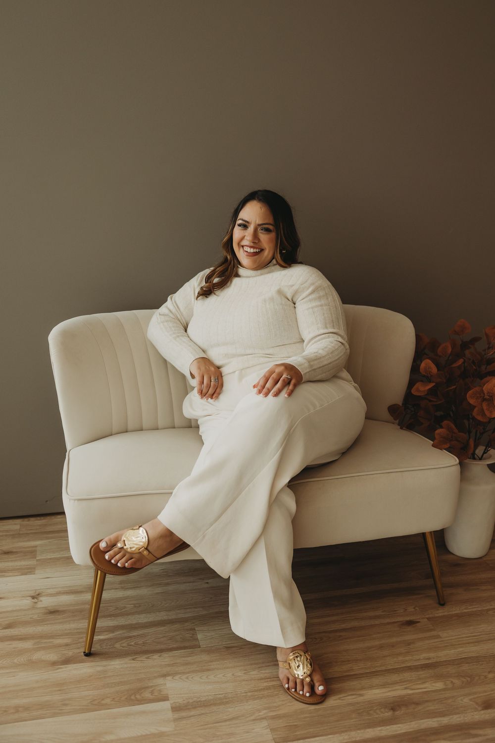 A person in a cozy white sweater and pants lounges on a cream-colored mid-century modern sofa in a minimalist setting.