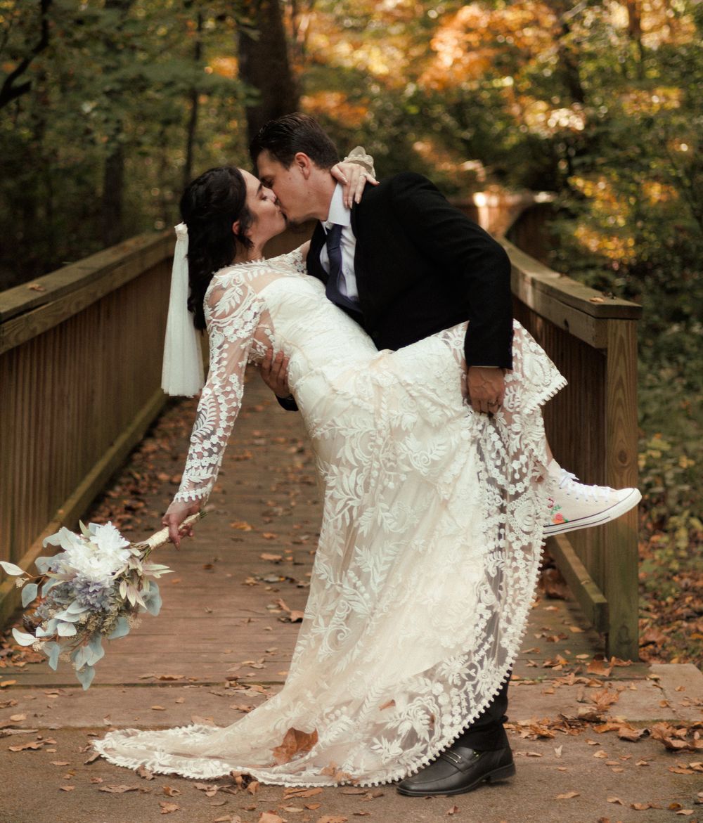 A bride and groom share a dip kiss at the end of the walkway. Her sneakers are visible under her dress