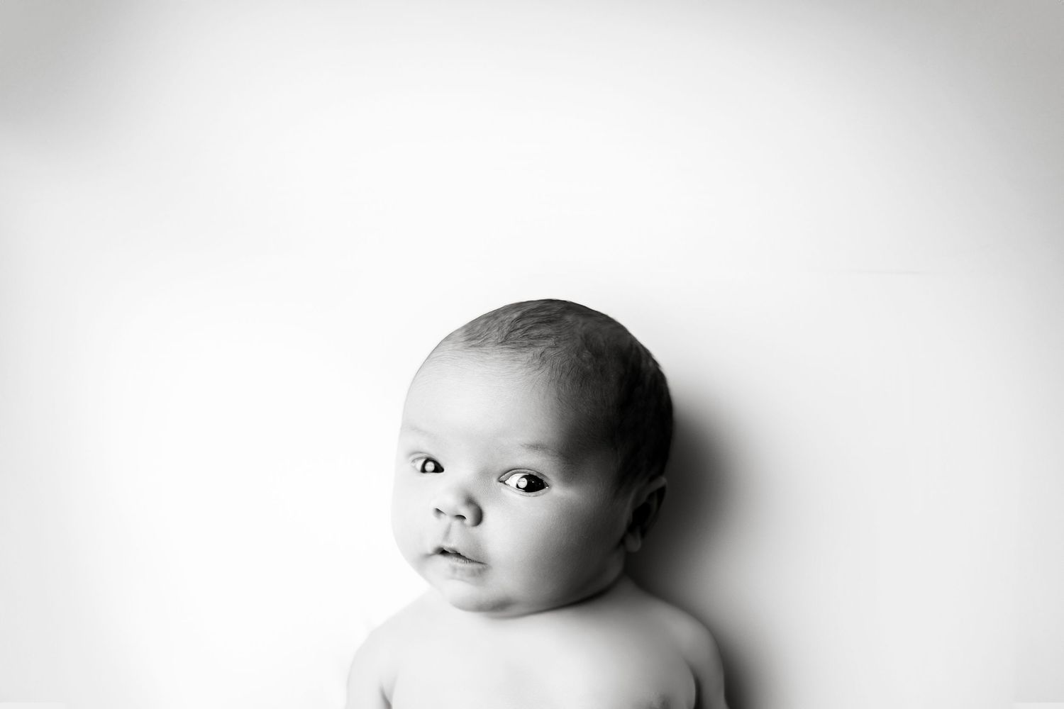Black and white artistic portrait of an infant looking to the side with soft lighting and blurred edges.