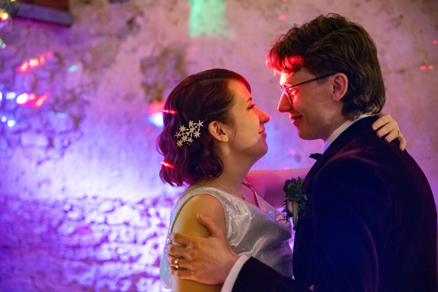Couple dances intimately under dramatic purple lighting at wedding reception.