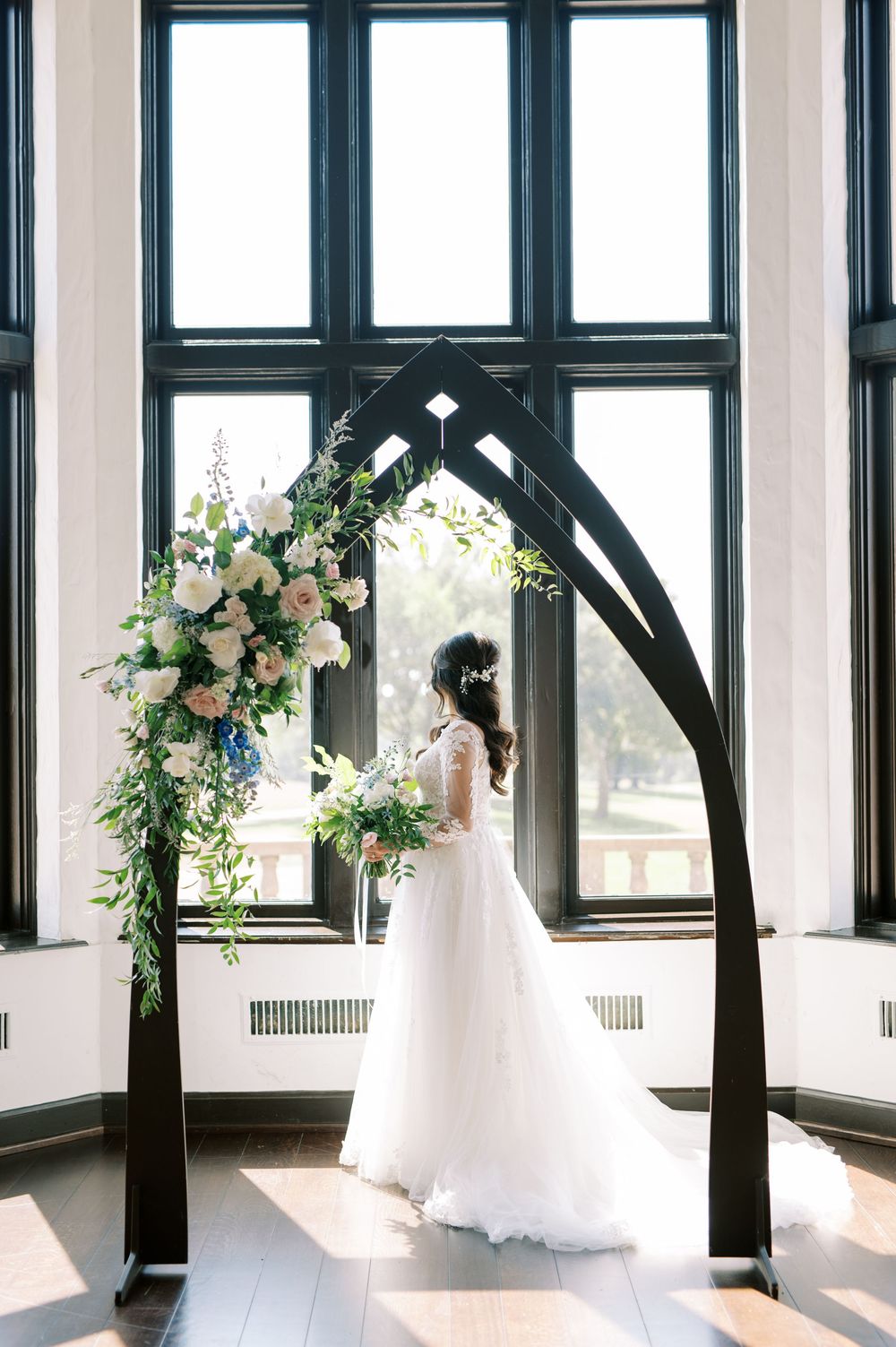 Panoramic view of elegant wedding venue with tall black-framed windows and white floral arrangements.