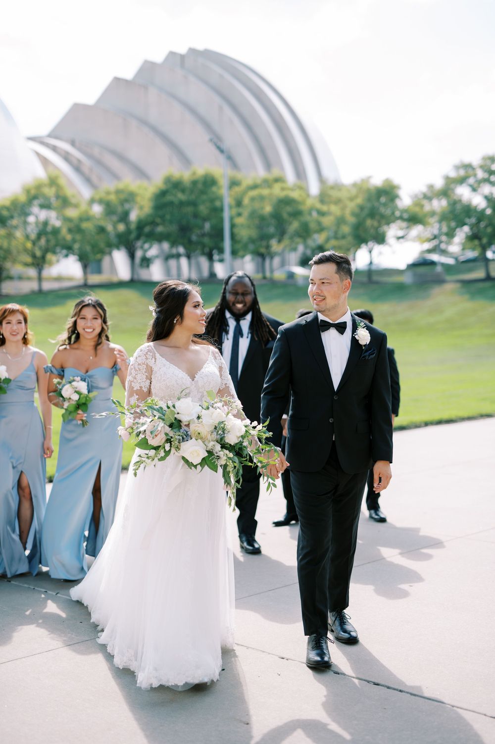 Wedding party walks together outside Kauffman Center for Performing Arts with its distinctive curved architecture.